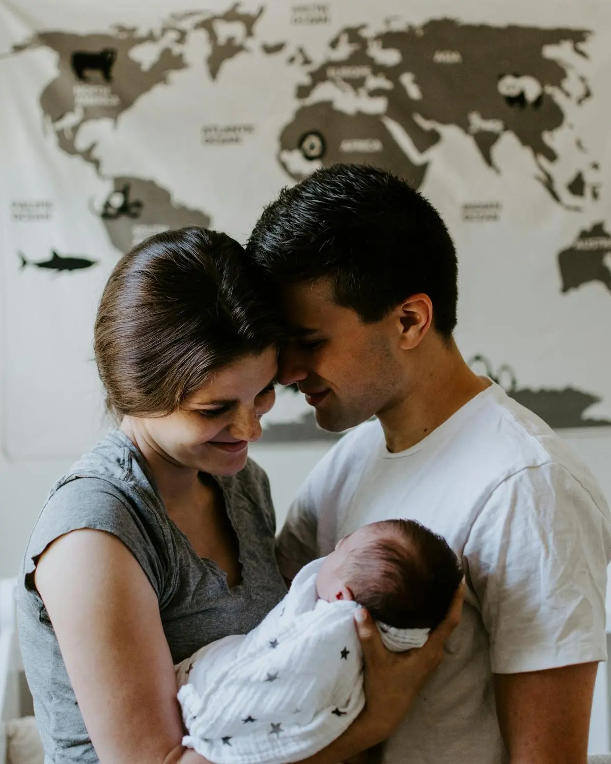 Young parents holding their newborn baby in front of a world map